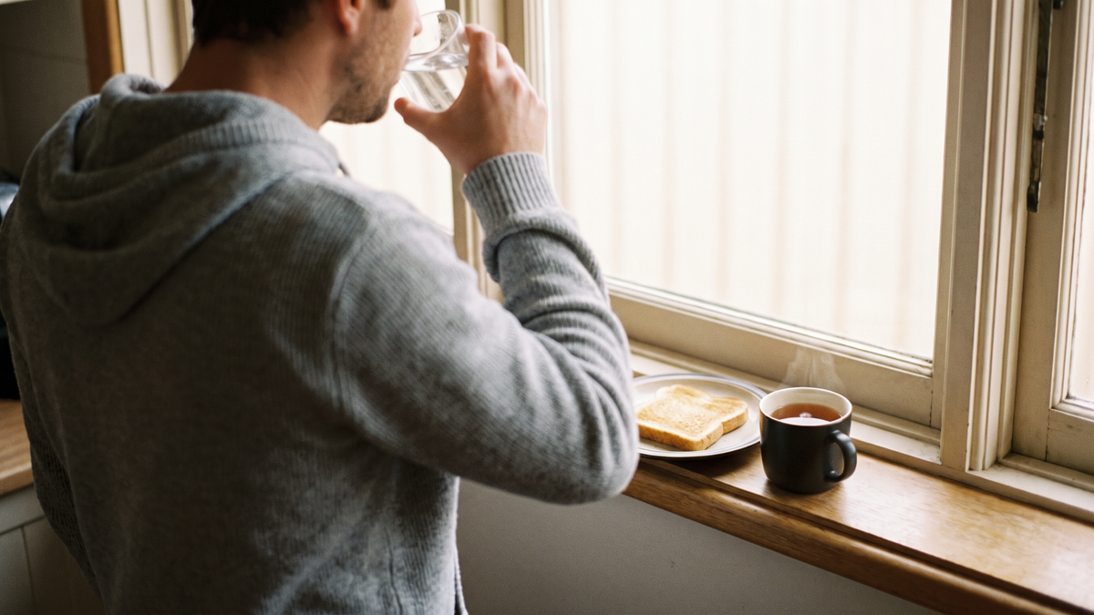 A man drinking water beside a window