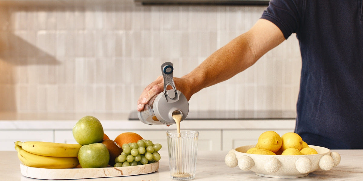 A man in his fifties at a marble kitchen bench pouring from a HLTH+ electric shaker into a glass — HLTH+