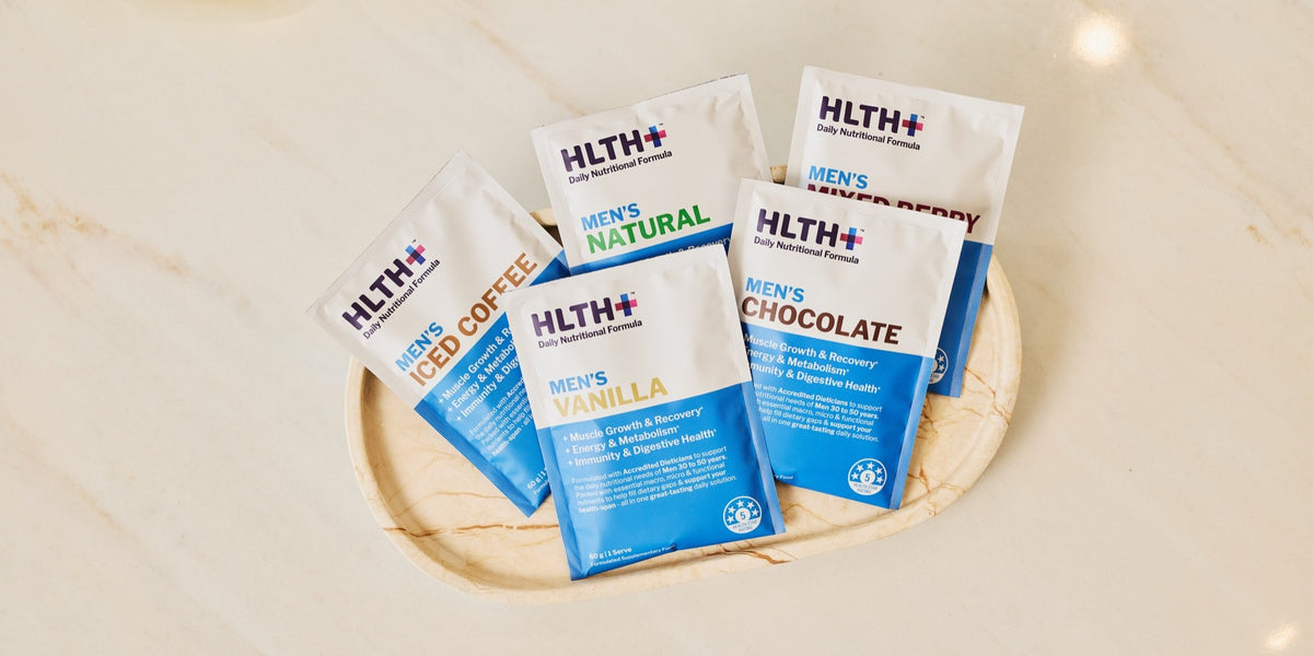 Five HLTH+ Men's sachets in different flavours arranged on a round wooden coaster — HLTH+