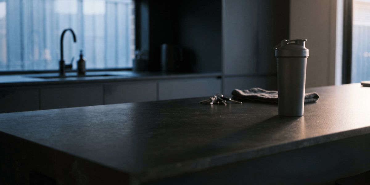 A grey shaker on a dark stone kitchen bench at dawn — HLTH+
