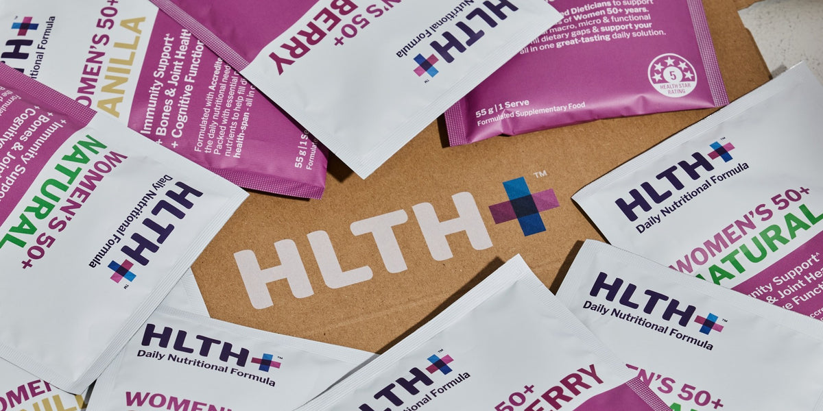 HLTH+ Women's 50+ Daily Nutritional Formula sachets in Chocolate and Mixed Berry fanned across a wooden surface — HLTH+