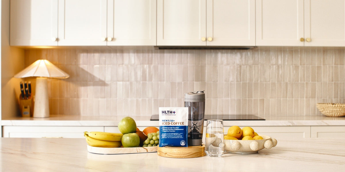 A HLTH+ Women's 50+ Iced Coffee sachet on a light marble benchtop in a modern kitchen — HLTH+