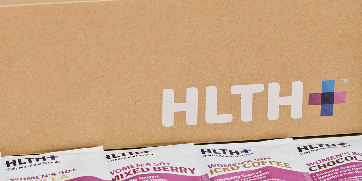 HLTH+ shipping box above four pink Women's 50+ Daily Nutritional Formula sachets on kraft paper — HLTH+