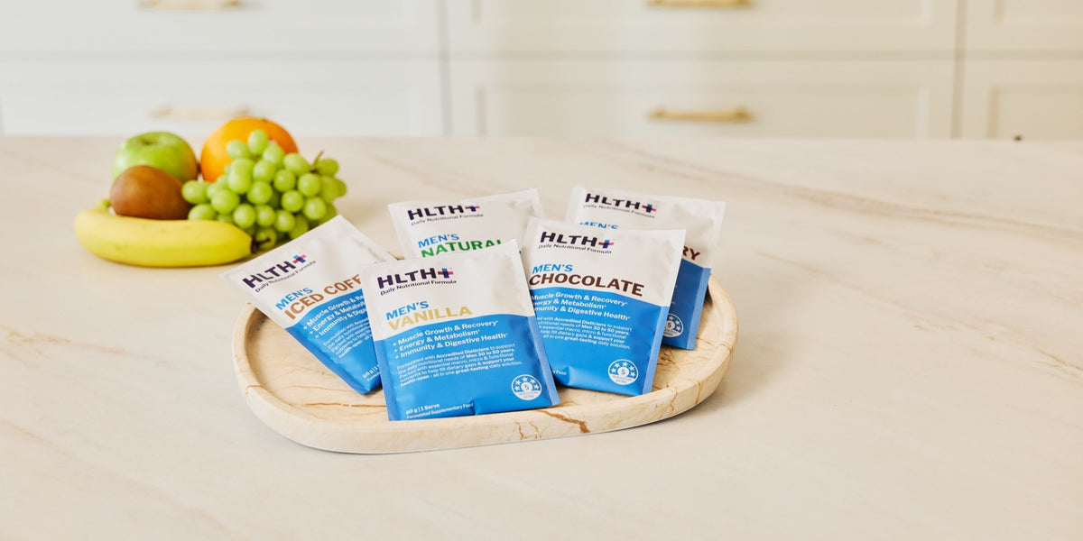 Three HLTH+ Men's sachets in different flavours arranged on a natural wooden surface — HLTH+