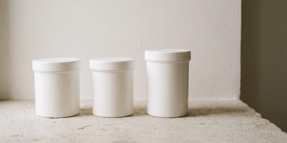 Three unbranded white powder tubs side by side on a light stone surface — HLTH+